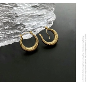 Detail of golden C-shaped titanium earrings with snake scale embossed texture on black surface