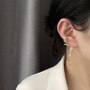 Eleganter goldener Blumen-Ohrclip mit Quasten am Model vor dunklem Hintergrund