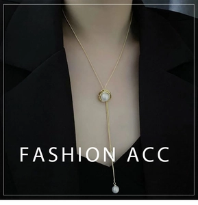 Détail d'un collier lasso doré avec perles et chaîne réglable sur un blazer noir