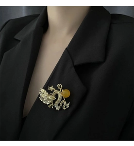 Detalle de broche de dragón dorado con pavé de cristales y cuenta amarilla en solapa negra