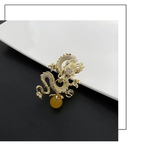 Detalle de broche de dragón dorado con cristales y perla amarilla sobre fondo dividido