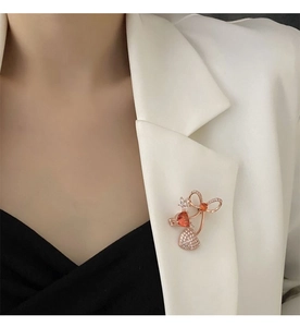Detail of rose gold bow brooch with orange heart zircon on white suit jacket
