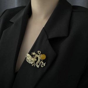 Elegante broche de dragón dorado con perla amarilla prendido en una chaqueta de traje negra