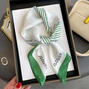 Elegant white silk scarf with green stripe trim and flower print tied on display board