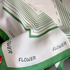 Detail of silk-like square scarf featuring green geometric patterns and flower lettering