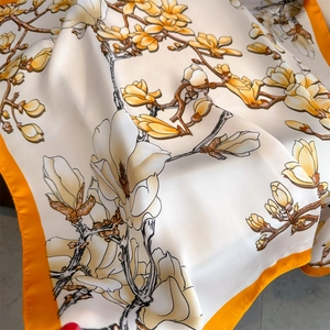 Detailed view of silk square scarf featuring yellow magnolia prints and orange borders