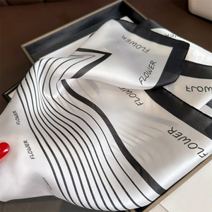 Detail of silk scarf showing black and white flower print with striped edge and glossy texture