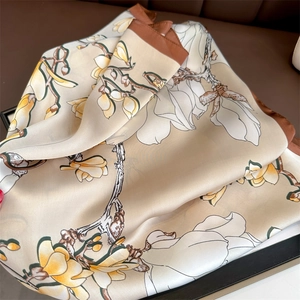 Detail showing elegant magnolia flower print on beige silk scarf with dark brown border