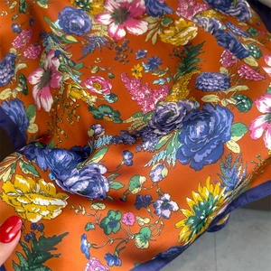 Detail showing the floral print on a silk square scarf with vibrant orange background