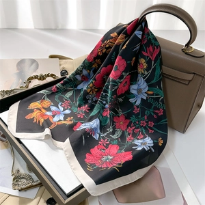 Floral print silk square scarf draped over a brown leather bag on a vintage tray