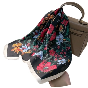 Black floral silk scarf with red poppies and blue lilies draped on a brown leather handbag