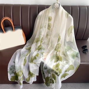 Elegant white chiffon scarf with green ginkgo leaf print displayed on a sofa