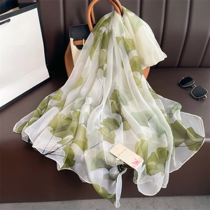 Elegant white silk scarf with green ginkgo leaf pattern draped over a leather handbag