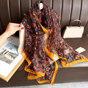 Elegant floral silk-like scarf with black base and red flowers on a leather sofa