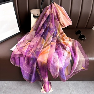 Elegant purple and orange floral gradient silk scarf draped on a stylish beige handbag