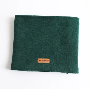 Détail d'un cache-cou en tricot vert foncé avec écusson en cuir et maille texturée