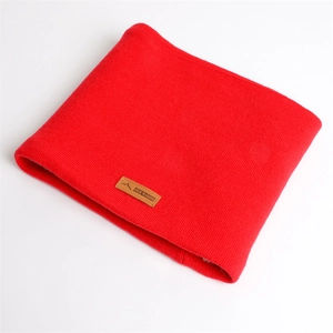 Détail d'un tour de cou en tricot rouge avec texture côtelée et écusson en cuir