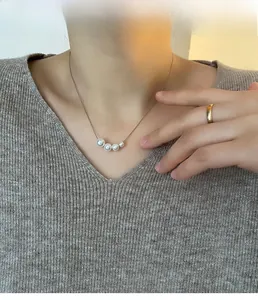 Detail view of graduated pearl pendant necklace worn on neck with elegant grey knitwear