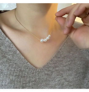 Close-up of elegant gold necklace with five graduated pearls on a grey knit top