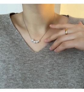Detail of elegant gradient faux pearl necklace on model with grey knit V-neck sweater