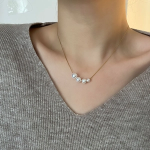 Minimalist gold necklace with four gradient pearls on a model wearing grey knitwear