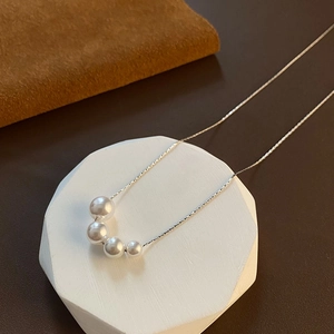 Minimalist silver necklace with four gradient pearls on a white geometric display stand