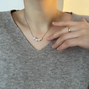 Minimalist pearl pendant necklace in silver chain worn by model with grey V-neck knitwear