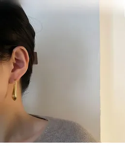 Close-up of minimalist gold long teardrop earrings showing elegant matte finish on model