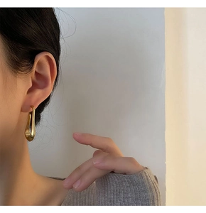 Close-up of minimalist gold teardrop earrings worn by model with soft shadow effects