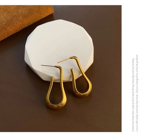 Detail of elegant gold U-shaped droplet earrings on a white minimalist display stand