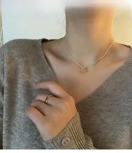 Gros plan d'un choker en perles avec pendentif fleur rose sur un mannequin en col V gris