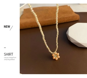 Détail du collier à perles avec fleur rose et centre vert sur une chaîne de perles