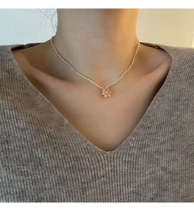 Détail d'un collier de perles florales avec perles dorées et pendentif fleur rose au cou