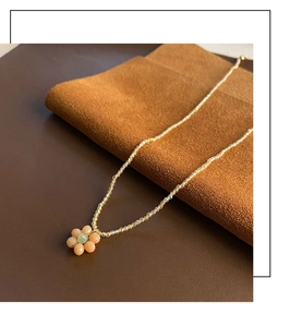 Détail d'un collier de fleurs en perles aux tons pastels sur un support en cuir chic