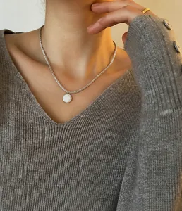Detailopname van een zilveren ketting met witte parelhanger gedragen door een model