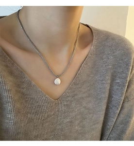 Detailopname van een zilverkleurige parelketting gedragen met een bruine gebreide trui