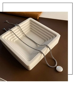 Detail van een zilveren getextureerde ketting met barokparel op een modern plateau