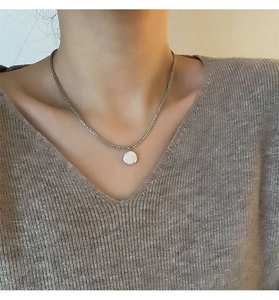 Detailopname van een zilveren ketting met een witte barokke parel op een beige trui