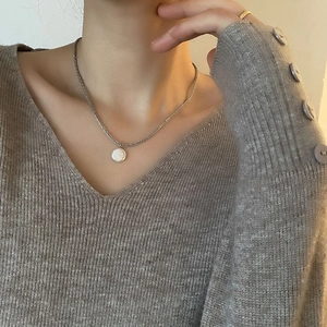 Elegante zilveren ketting met ronde witte parelhanger gedragen op gebreide trui