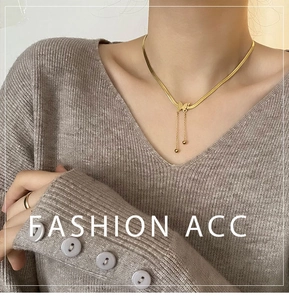 Détail du collier papillon doré 18K avec pompon sur mannequin en pull tricoté