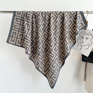 Close-up of geometric G-pattern printed silk scarf draped on a metal hanger