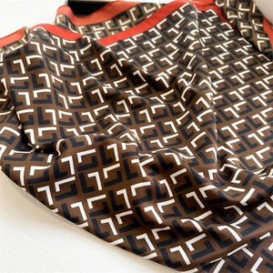 Macro detail of luxury silk scarf showing brown L-pattern print and orange border trim