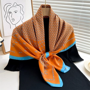 Orange fashion silk scarf with blue border and geometric letter print displayed on hanger