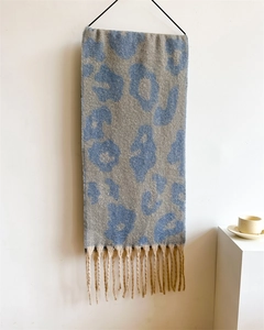 Detailaufnahme des Strickschals mit Leopardenmuster und langen Fransen an der Wand