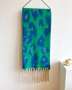Detail eines grünen Leoparden-Strickschals mit blauen Flecken und dicken Quasten