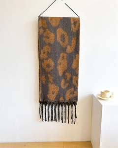 Detailansicht eines dicken Leoparden-Schals mit Fransen an einer minimalistischen weißen Wand