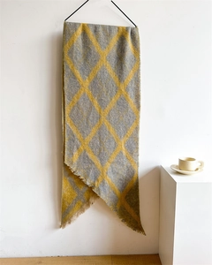 Détail d'une écharpe en maille argyle jaune et grise avec franges sur un cintre minimaliste