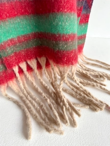 Close-up of striped knit scarf texture with red and green wool fibers and beige tassels