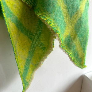 Gros plan sur une écharpe à carreaux vert et jaune avec texture polaire et longs franges