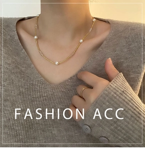 Gros plan d'un collier de perles françaises avec billes dorées sur un pull marron